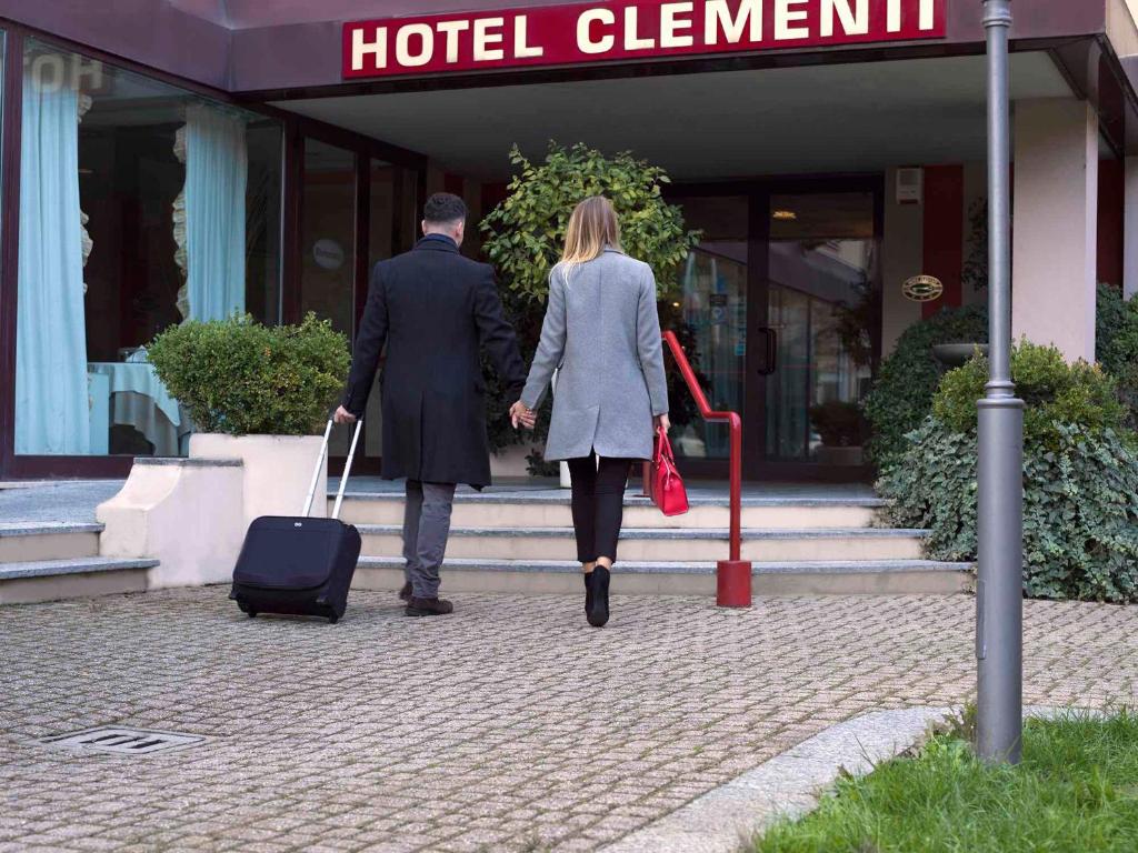 een man en vrouw die een hotel binnenlopen met hun bagage bij Hotel Clementi in Salice Terme