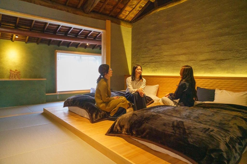 3 Frauen sitzen in einem Zimmer mit Betten in der Unterkunft SIMA inn in Onomichi