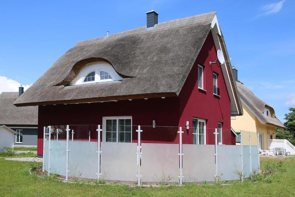 una casa roja con techo de gambrel con una valla blanca en Ferienhaus Lotsenhaus am Breetzer Bodden in Vieregge, en Vieregge
