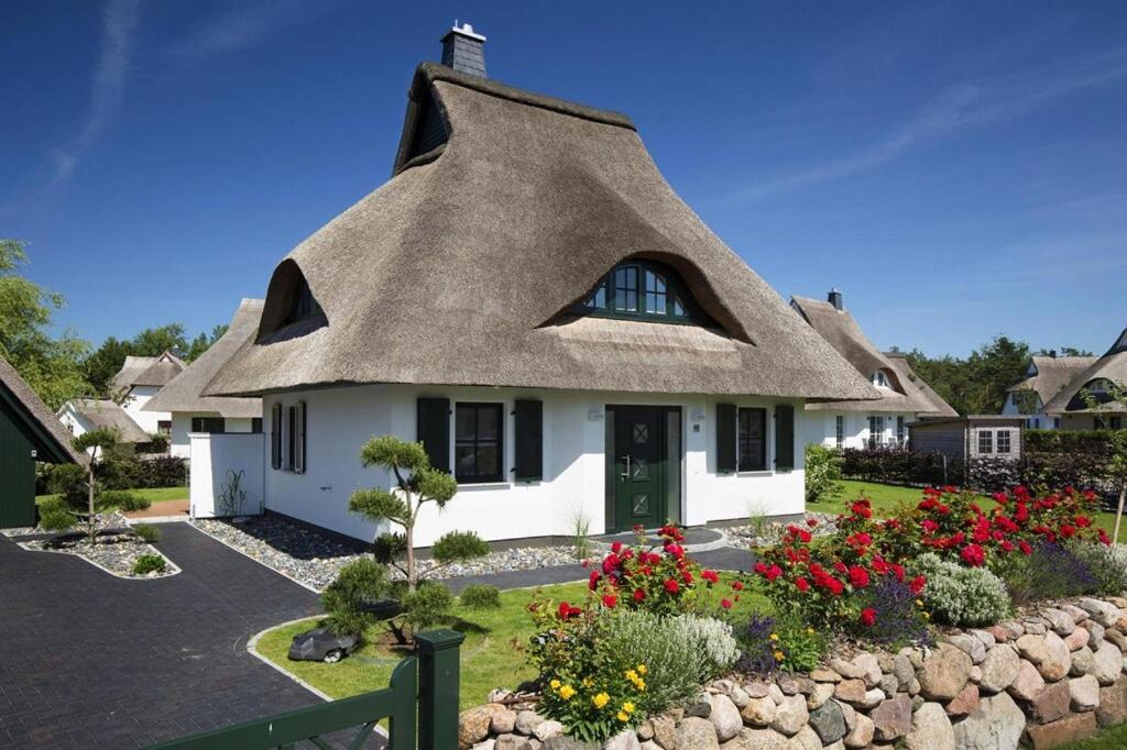 a thatch roof house with flowers in front of it at Holiday house, Fuhlendorf in Fuhlendorf