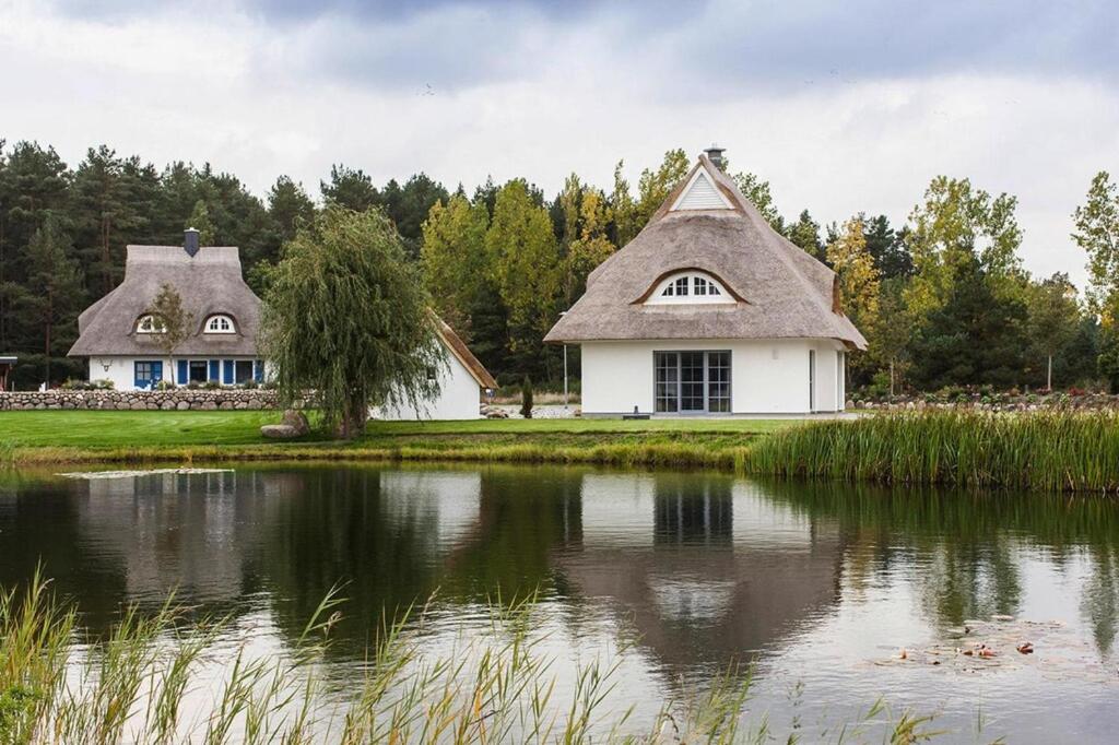 a house with a thatched roof next to a pond at Holiday house, Fuhlendorf in Fuhlendorf