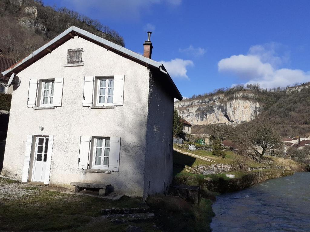 una casa blanca con un banco junto a un río en Gite Le bout du monde, en Baume-les-Messieurs