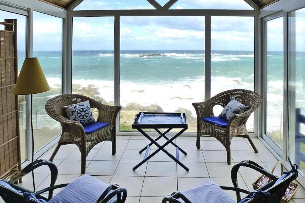 un porche grillagé avec des chaises et une table et l'océan dans l'établissement Fisherman's House in Brittany by the Sea, à Plouescat