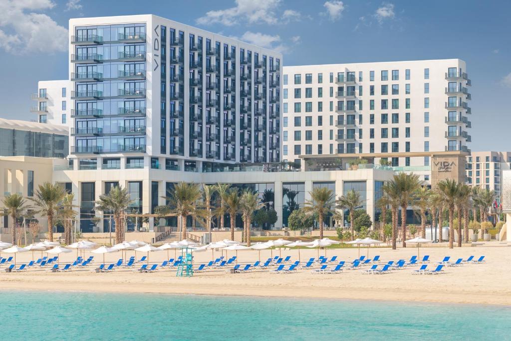 Vida Beach Resort Marassi Al Bahrain في المنامة: شاطئ يوجد فيه كراسي الشاطئ والمباني في الخلف