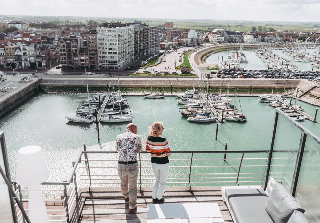 2 personas de pie en un balcón con vistas al puerto deportivo en ZEEPAREL Duplex loft, en Blankenberge