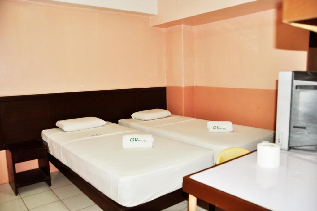 2 Betten in einem kleinen Zimmer mit einem Tisch in der Unterkunft GV Hotel - Lapu-Lapu City in Mactan