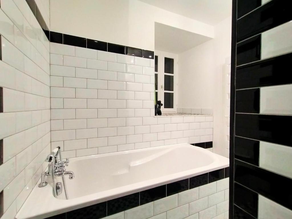 a white bath tub in a bathroom with black tiles at Gîte Eloquent in Gratot
