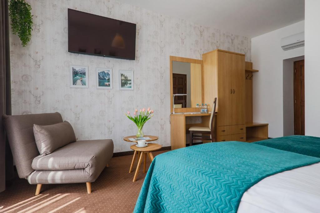 Calm hotel bedroom with teal bedspreads, chaise lounge, dresser with mirror and wall TV.