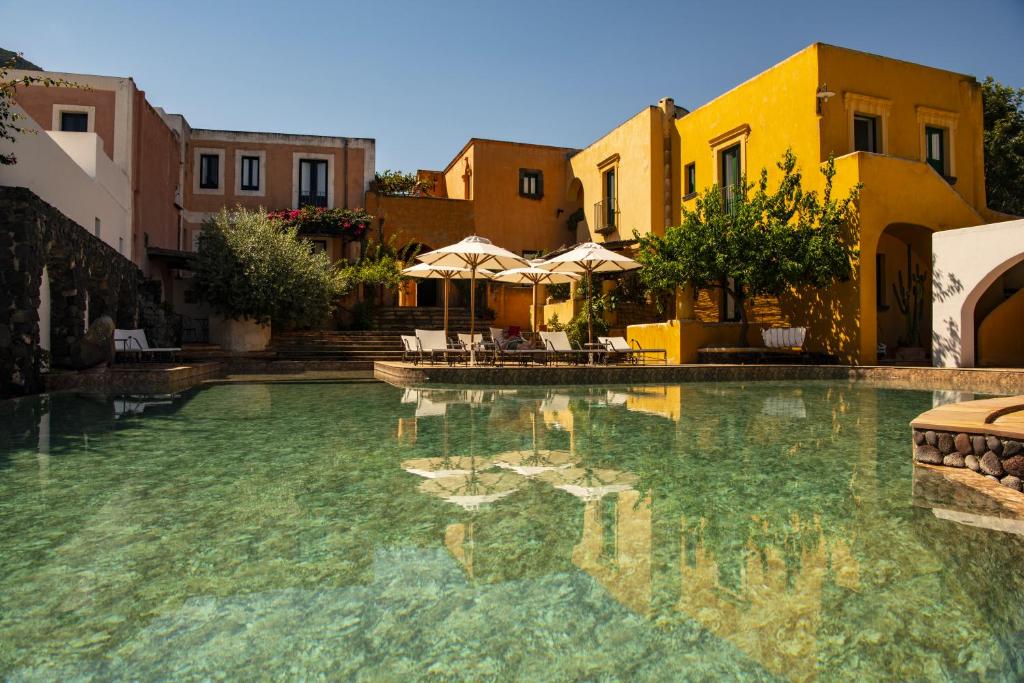 a swimming pool with chairs and umbrellas and buildings at Hotel Signum in Malfa