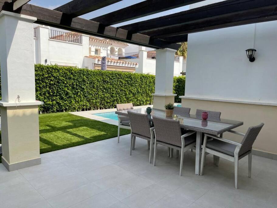 a patio with a table and chairs and a garden at Fantastica villa con piscina en gran golf resort in Roldán