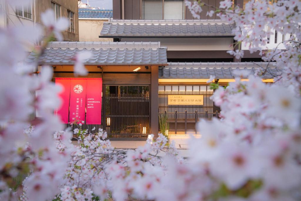 a building with a red sign in front of it with pink flowers at Kyoto Takasegawa Bettei in Kyoto