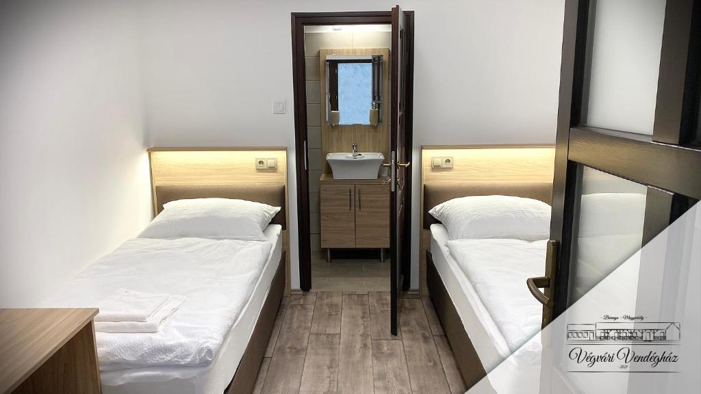 two beds in a room with a sink and a mirror at Végvári Vendégház in Magyarbóly