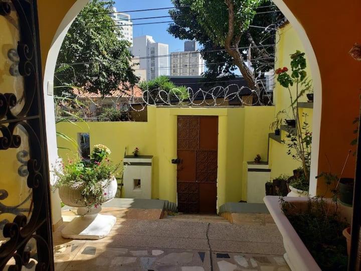 een ingang naar een geel huis met een deur bij Quarto com varanda em casa próxima a área hospitalar em BH in Belo Horizonte