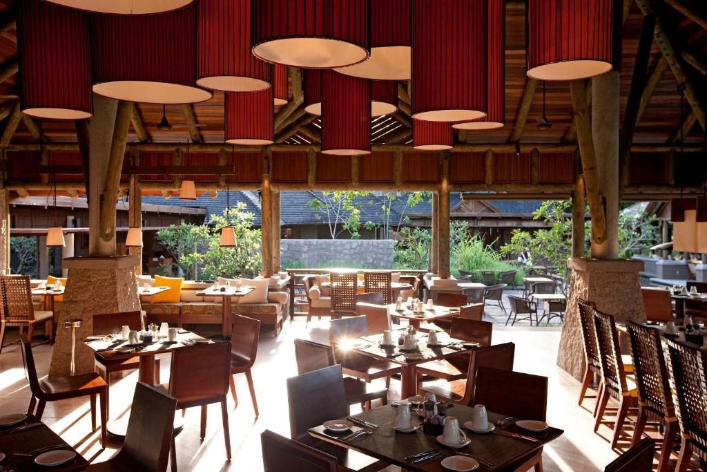 a restaurant with wooden tables and chairs and red curtains at Constance Ephelia in Port Glaud