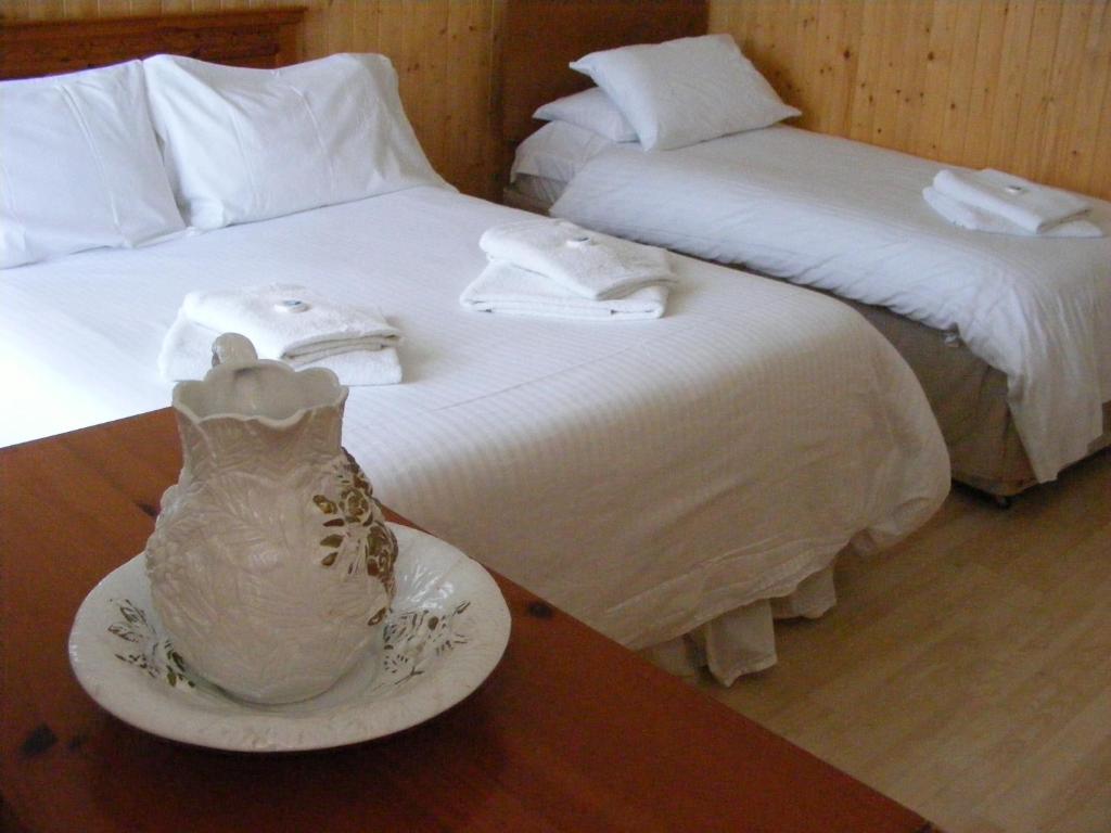 two beds with white sheets and a vase on a table at Trevelyan Hotel in Douglas