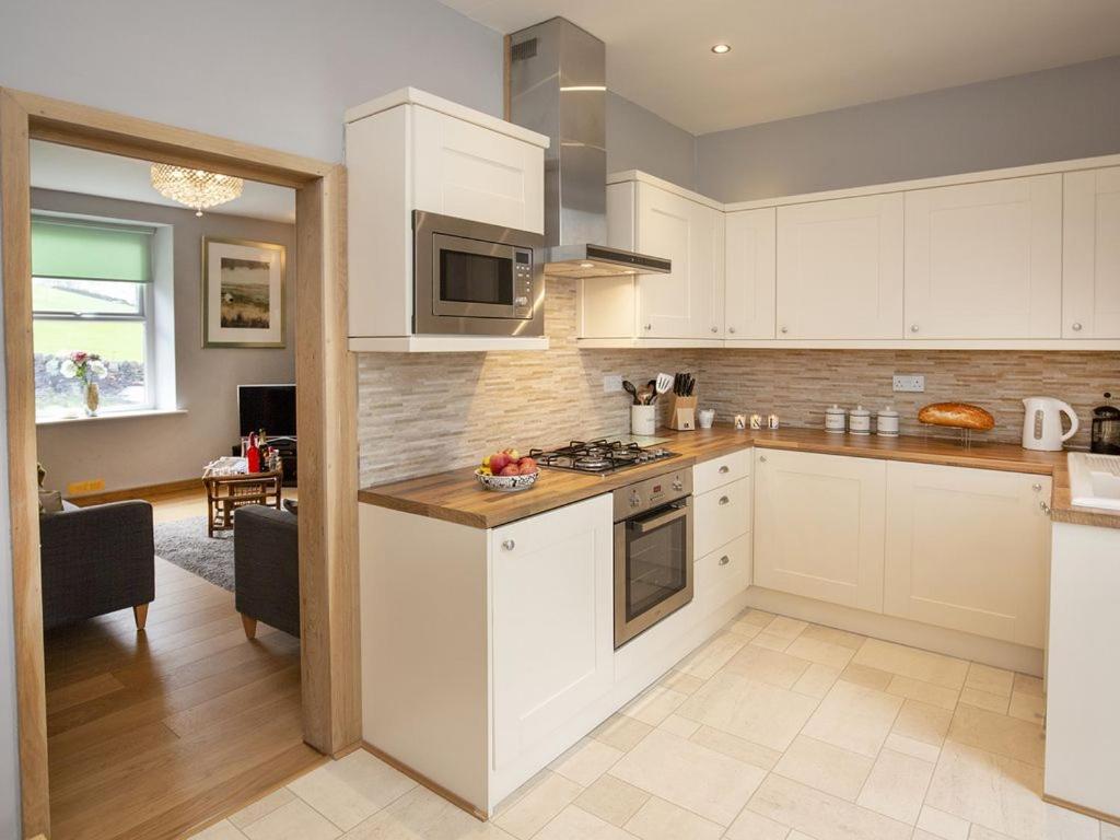 a kitchen with white cabinets and a stove top oven at The Yorkshire Hosts - Fall in Green Cottage in Haworth