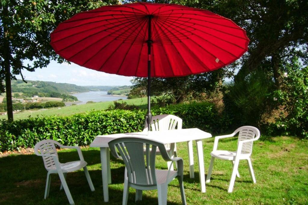 Trégarvanにあるholiday home, Trégarvanの赤い傘付きテーブルと椅子