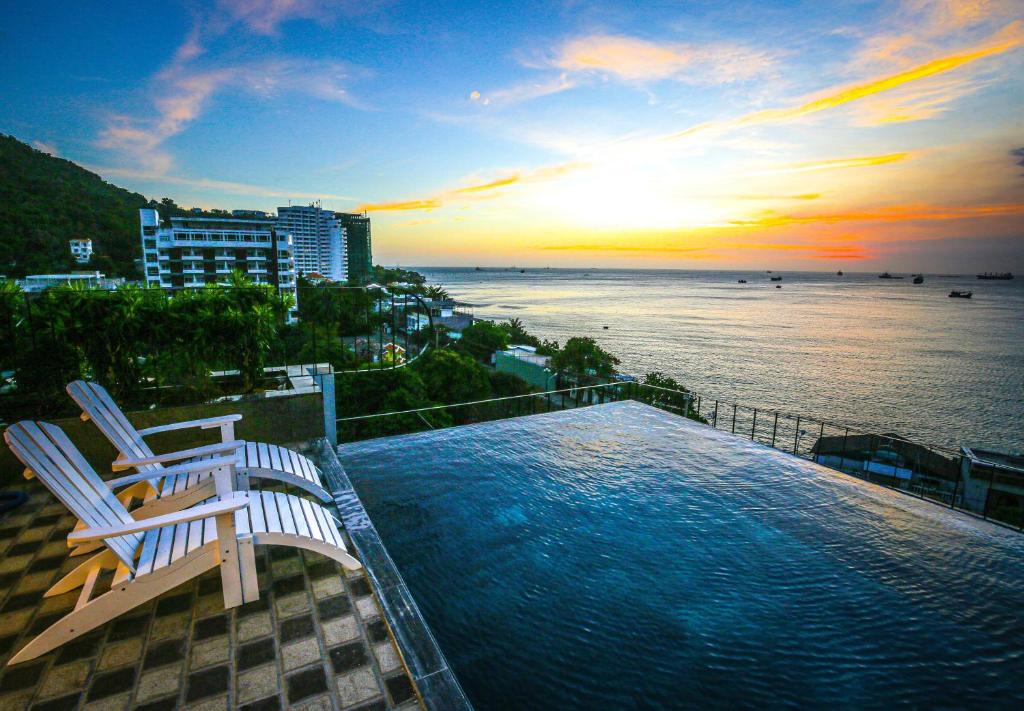 een zwembad met twee stoelen en de oceaan bij zonsondergang bij Fati Boutique Hotel & Apartment in Vung Tau