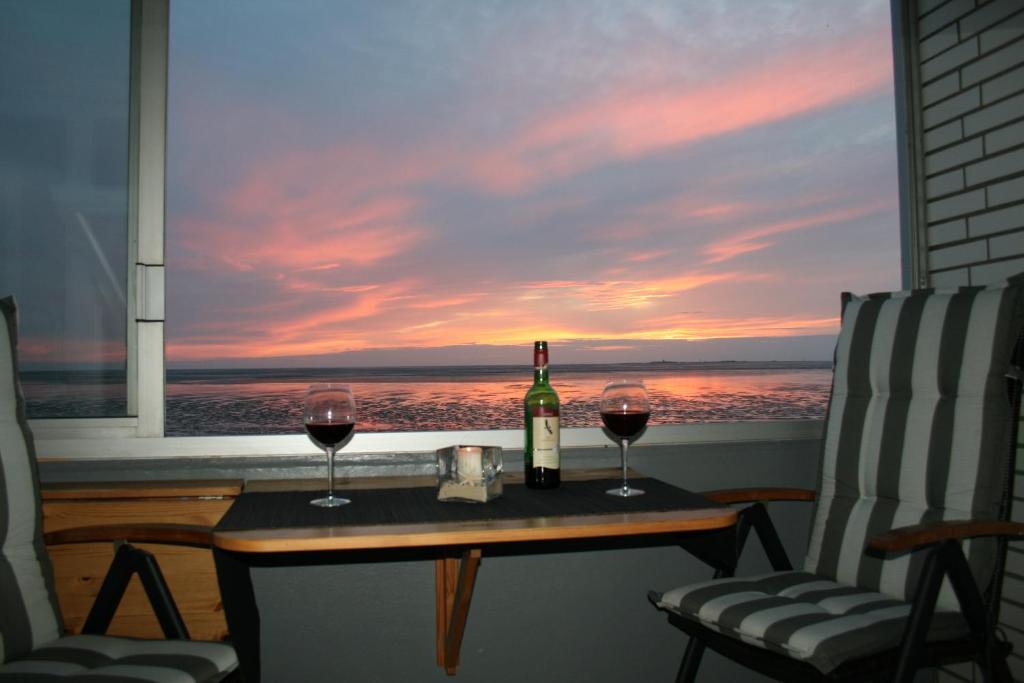 eine Flasche Wein und zwei Gläser auf einem Tisch vor einem Fenster in der Unterkunft Watten-Blick 1 in Cuxhaven