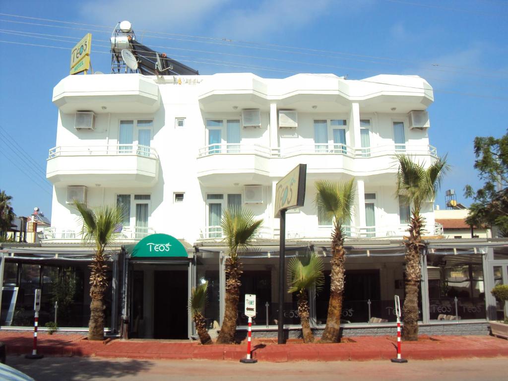 a white building with palm trees in front of it at Teos Hotel in Antalya