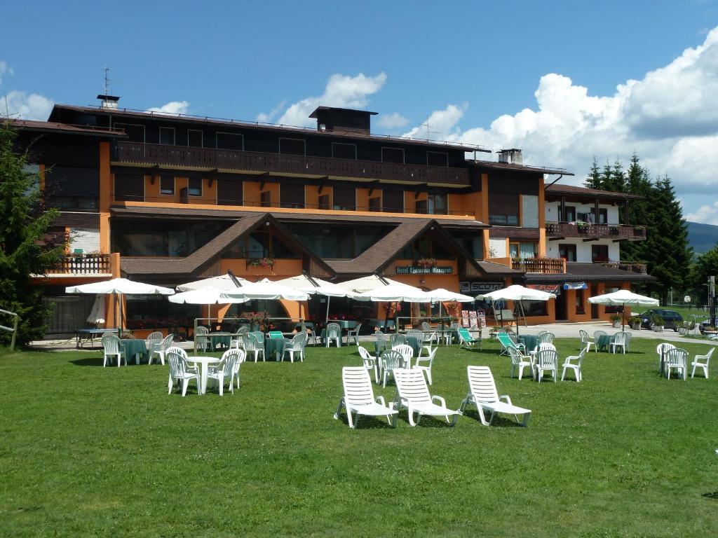 a building with white chairs and umbrellas in the grass at Albergo Miramonti Dependance in Asiago
