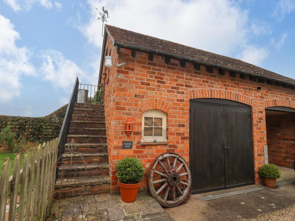 a brick building with a wooden door and a wheel at The Loft Room in Dymock