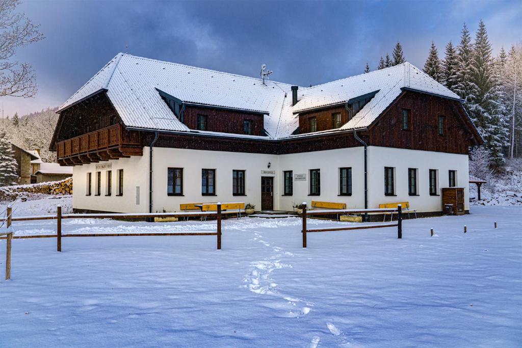 ein großes Holzgebäude mit Schnee auf dem Boden in der Unterkunft Dvůr Lískový vrch in Strážný