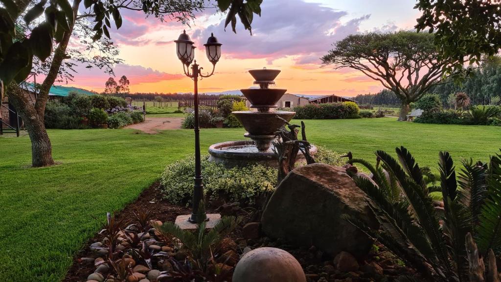 a fountain in a yard with a sunset in the background at Forest Hill Country Lodge in Piet Retief
