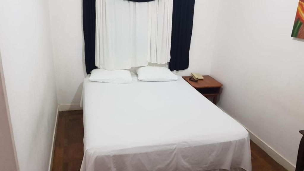 a bedroom with a bed with white sheets and a window at Hotel Itapetininga in Itapetininga
