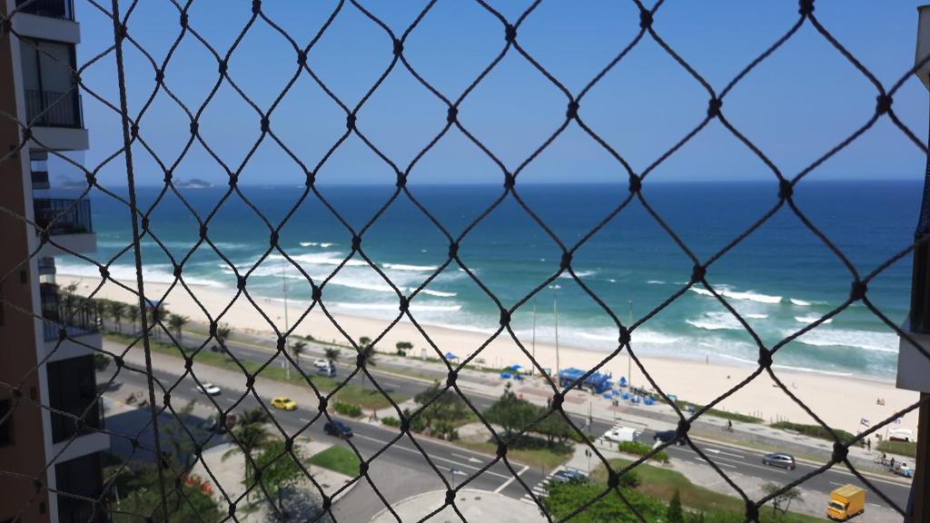 einen Blick auf einen Strand durch einen Zaun mit Kettenglieder in der Unterkunft Flat 2 suites com vista para o mar e lagoa. in Rio de Janeiro