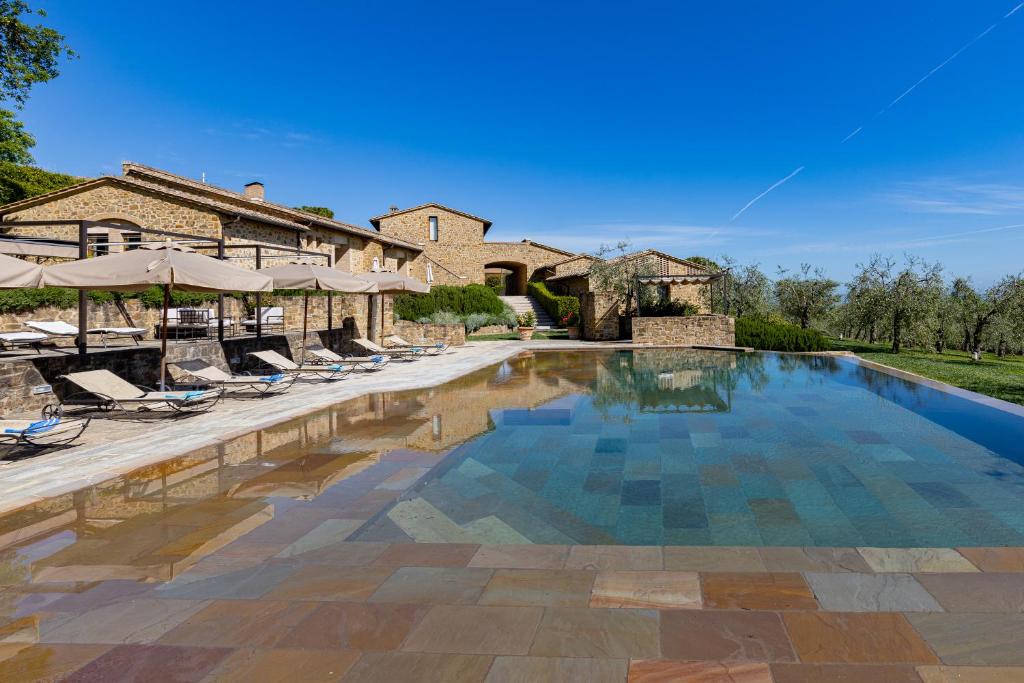 a swimming pool with chairs and umbrellas in front of a house at Borgo Canalicchio Di Sopra Relais in Montalcino