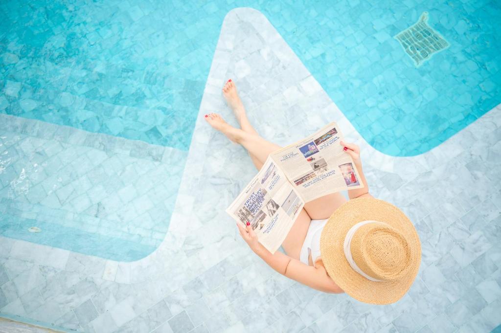a woman in a hat reading a newspaper next to a swimming pool at Veranda Residence by GoldStar Group in Jomtien Beach