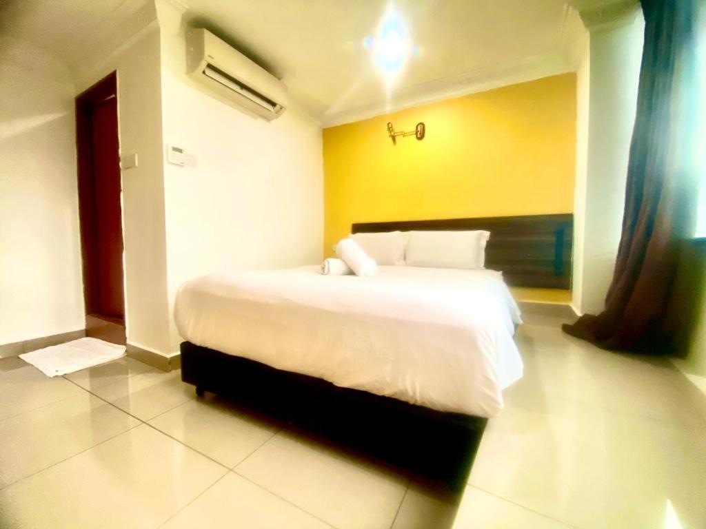 a bedroom with a large white bed with a yellow wall at N HIBISCUS HOTEL in Seri Kembangan
