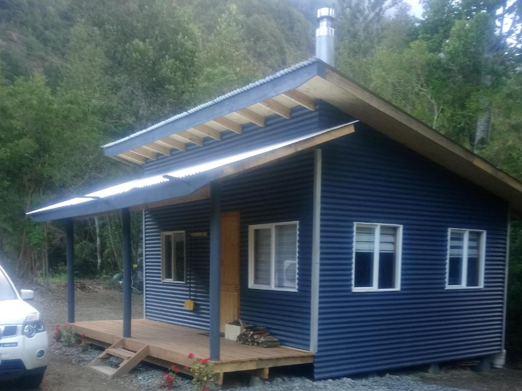 ein blaues Haus mit einer Veranda und einem Dach in der Unterkunft Cabañita Sustentable El Este Cochamó in Cochamó