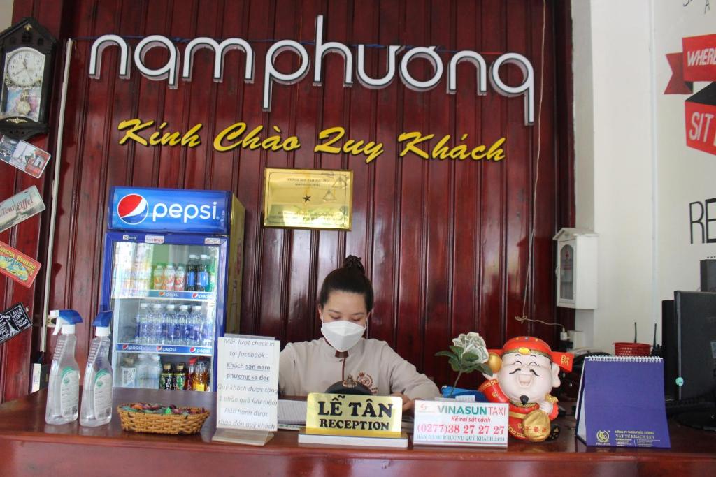 Una mujer con una máscara detrás de un mostrador en una tienda en Nam Phương Hotel Sa Đéc en Sa Ðéc
