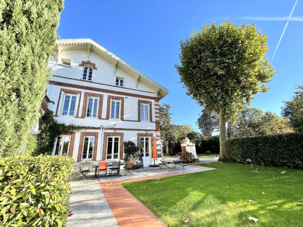 uma grande casa branca com um relvado e árvores em La Mélanotte em Toulouse