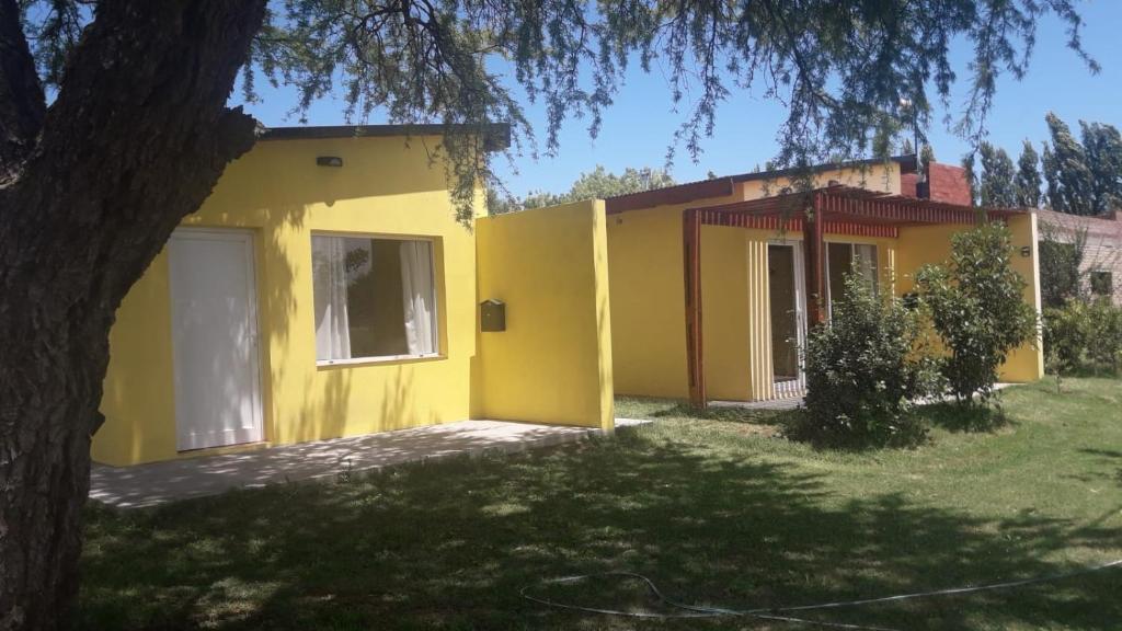 Una casa amarilla con un árbol delante. en Departamento Teodelina en Quehué