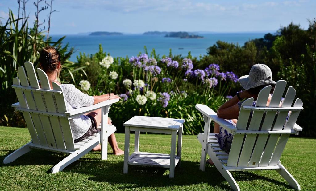 dos personas sentadas en sillas de césped en el césped en Kākā Ridge Retreat Luxury Cottage, en Tawharanui