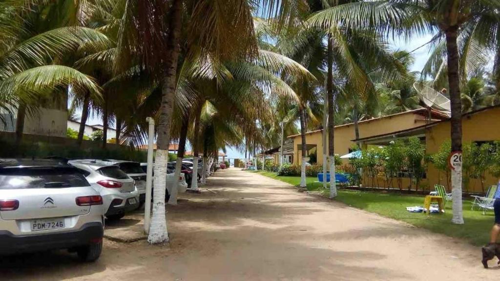 a street with cars parked next to palm trees at Casa Logan - Condomínio Village, Casa 15 in Maragogi