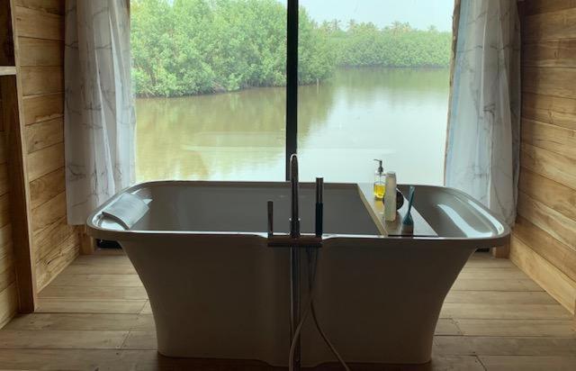 a bath tub in a room with a view of a river at Natura Luxury Lake Hut in Ouidah