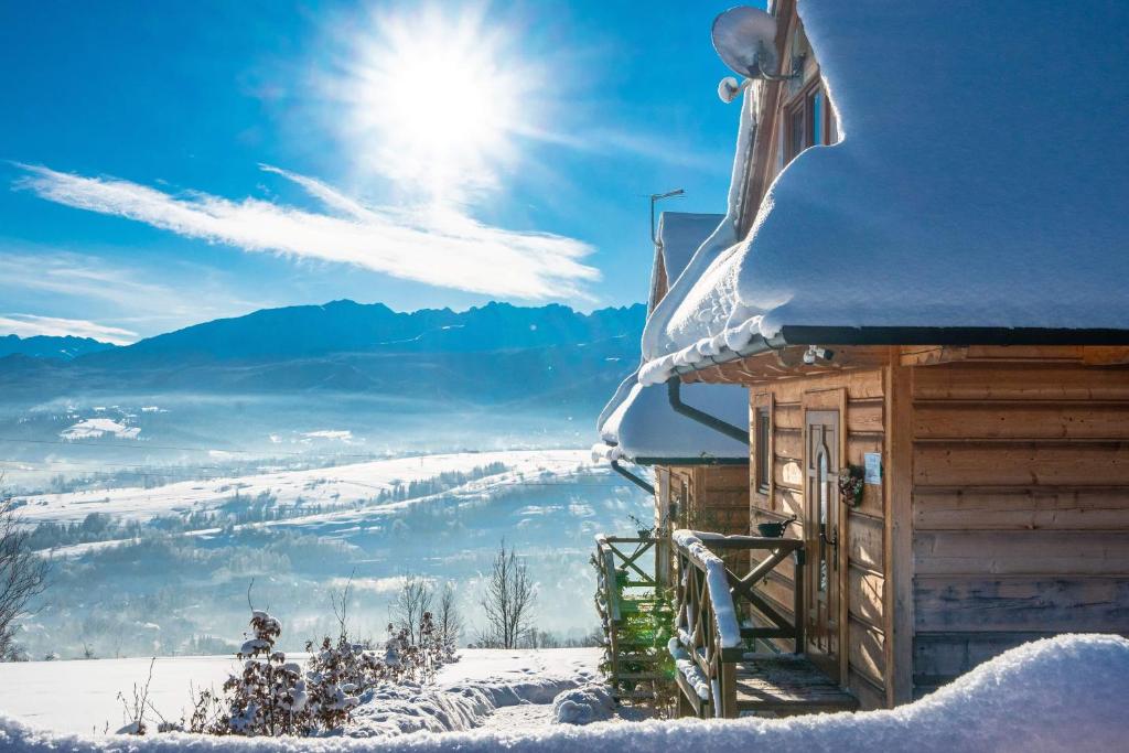 a snow covered cabin with the sun in the background at Domki Widokowe Wooden Luxury Chalet in Ząb
