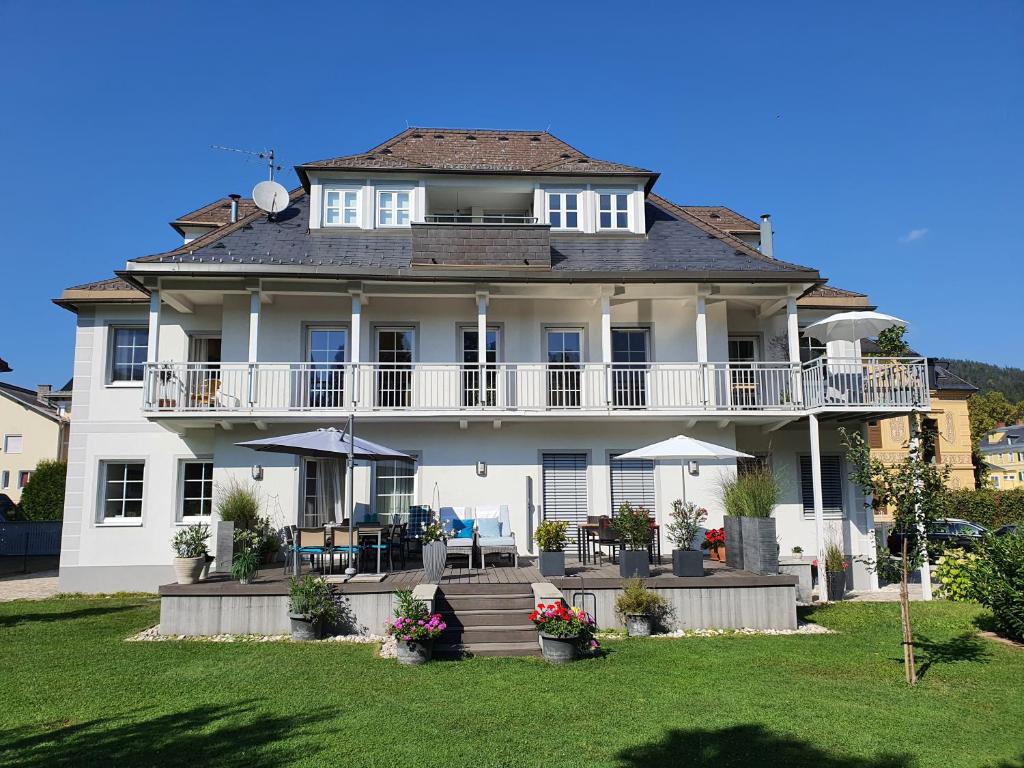 Großes weißes Haus mit Balkon und Rasen in der Unterkunft Villa Wieser in Pörtschach am Wörthersee