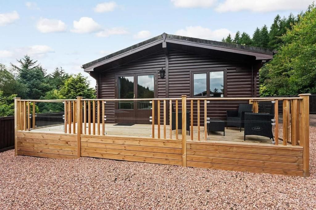 eine Hütte mit einer Holzterrasse mit einem Zaun in der Unterkunft Corrie Lodge, Glendevon in Glendevon