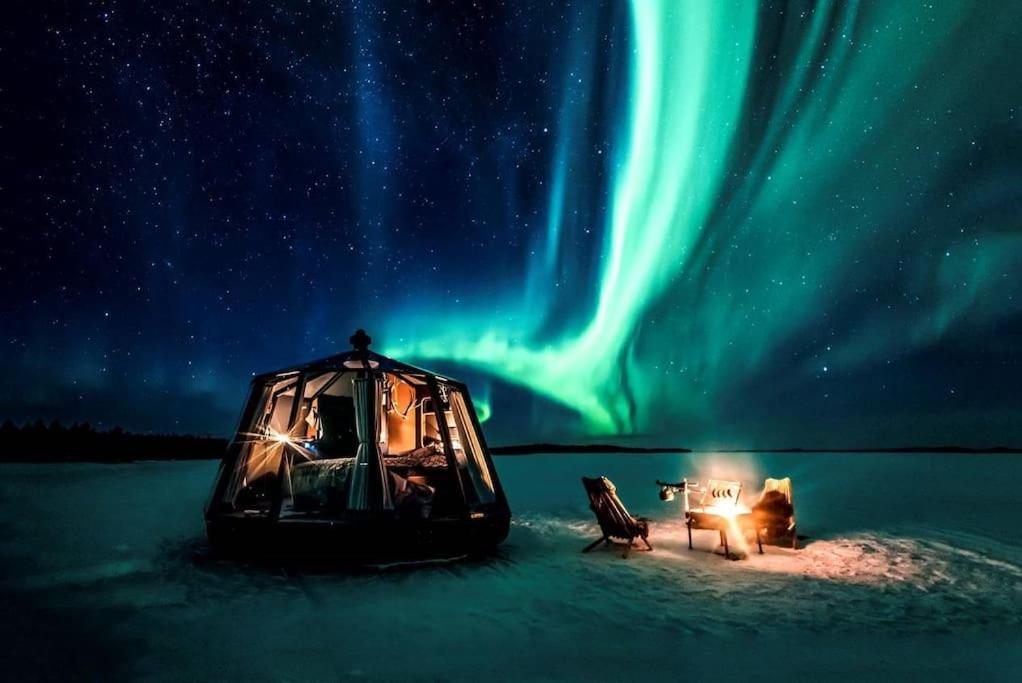 ein Zelt und ein Tisch und Stühle im Schnee unter den Nordlichtern in der Unterkunft Northern Lights Glass Igloo Getaway For Couples in Rovaniemi