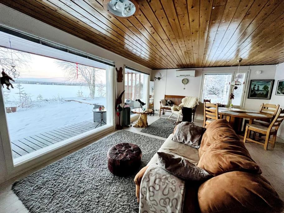 a living room with a large couch and a large window at Lapland Sunrise Cottage with lakefront Sauna in Rovaniemi