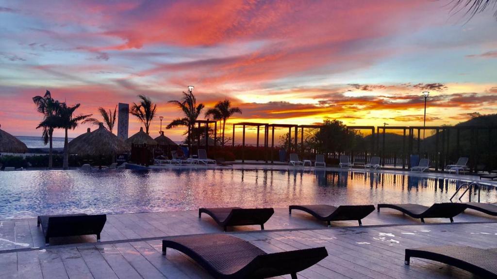 a pool with chairs and a sunset in the background at Apartamento en Santa Marta - Samaria junto a la Playa Pozos Colorados in Gaira