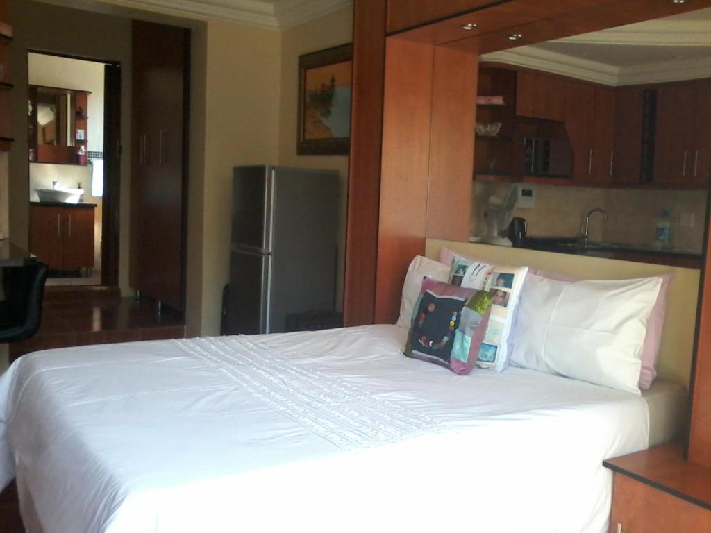 Schlafzimmer mit einem weißen Bett und einem Kühlschrank in der Unterkunft Genie's Nest 4 in Pretoria