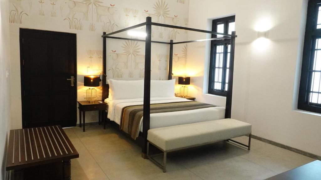 a bedroom with a four poster bed and a bench at Jetwing Mahesa Bhawan in Jaffna