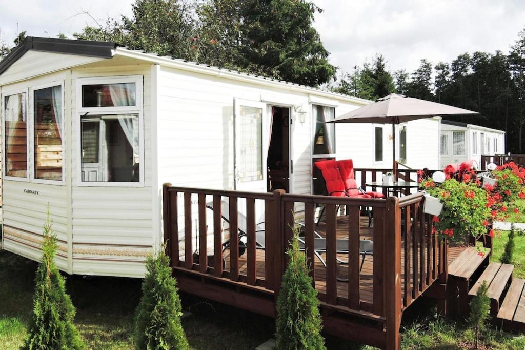 a white caravan with a deck and an umbrella at Mobile home in Kolczewo with a terrace in Kołczewo
