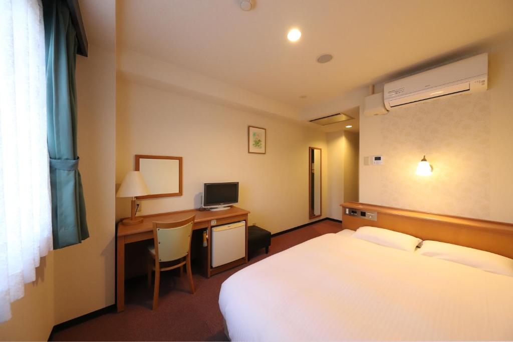 高岡市にあるスマイルホテル高岡駅前のベッド、デスク、コンピュータが備わるホテルルームです。